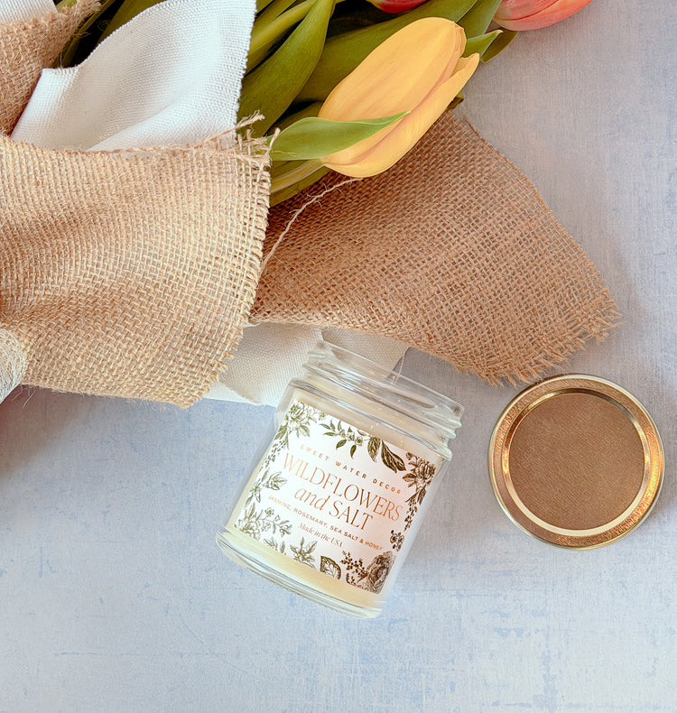 Candle jar labeled 'Wildflowers & Sea Salt' with a bouquet of flowers on a light background