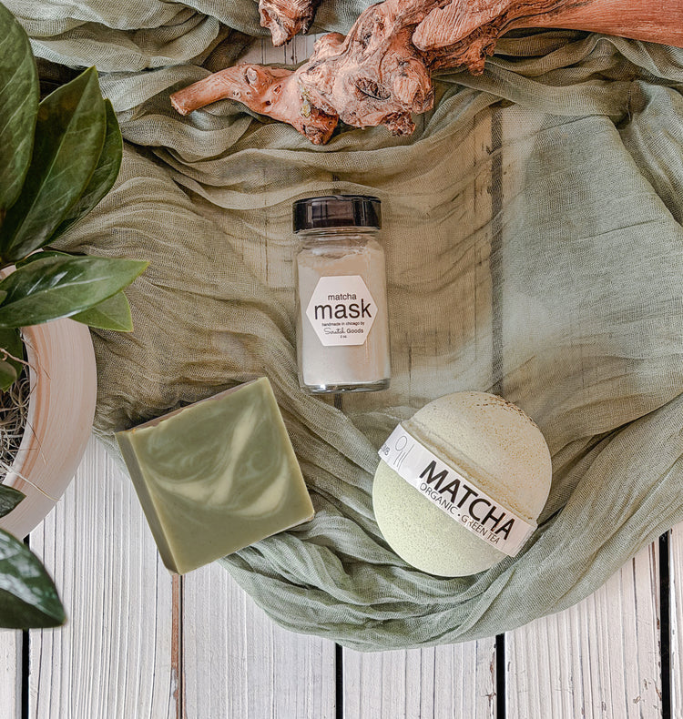Matcha-themed products including a bar of soap and a jar on a textured green fabric background.
